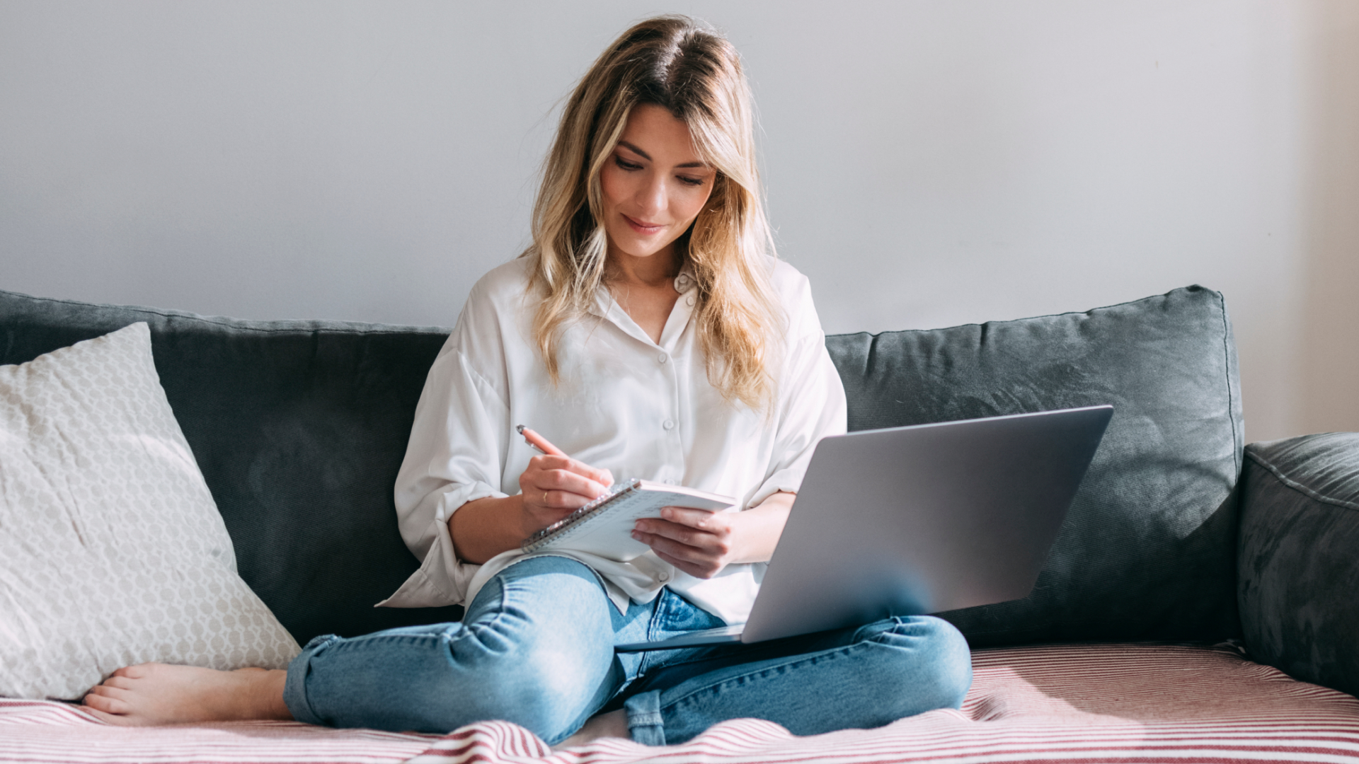 Woman writing notes while working at home with laptop.