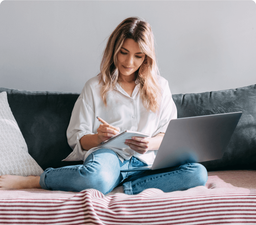 Woman writing notes while working at home with laptop.